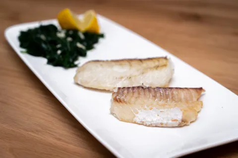Zwei goldbraun gebratene Fischfilets mit Blattspinat und Zitronenspalte