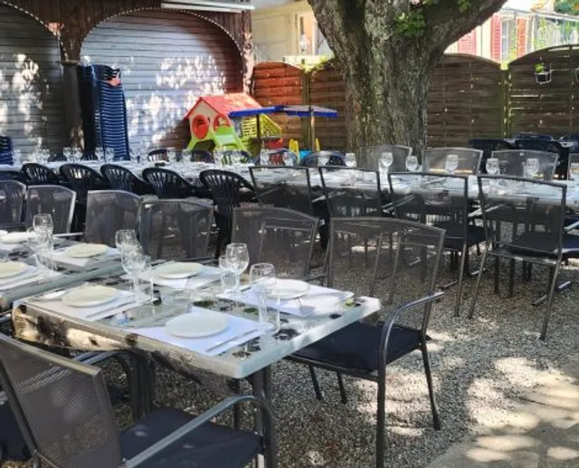 Terrasse mit langer Tischreihe unter Kastanienbäumen, im Hintergrund ein Kinderspielhaus