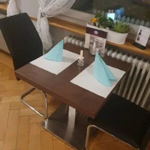 Eingedeckter Tisch mit türkisen Servietten vor einem Fenster mit weissem Spitzenvorhang